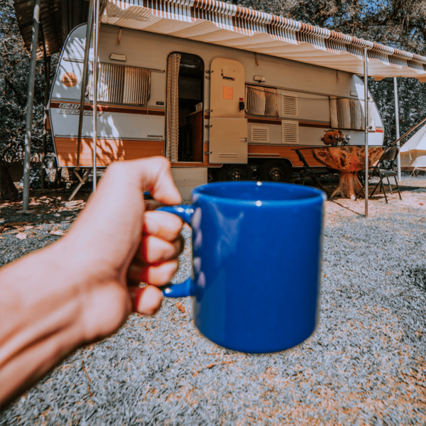 Person holding mug of coffee made with Lavazz decaf coffee beans in front of caravan